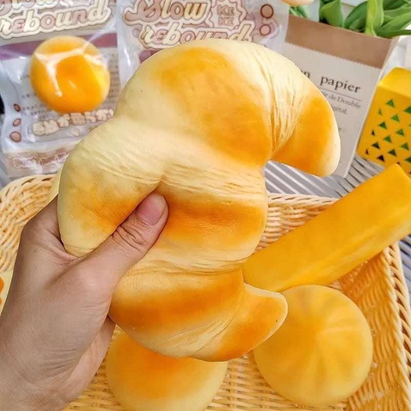 A hand holds a squishy croissant stress relief toy with orange and white stripes on a woven tray.