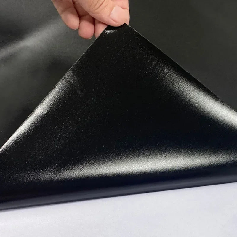 A hand is holding a black, triangular chalkboard wall sticker panel against a white surface.
