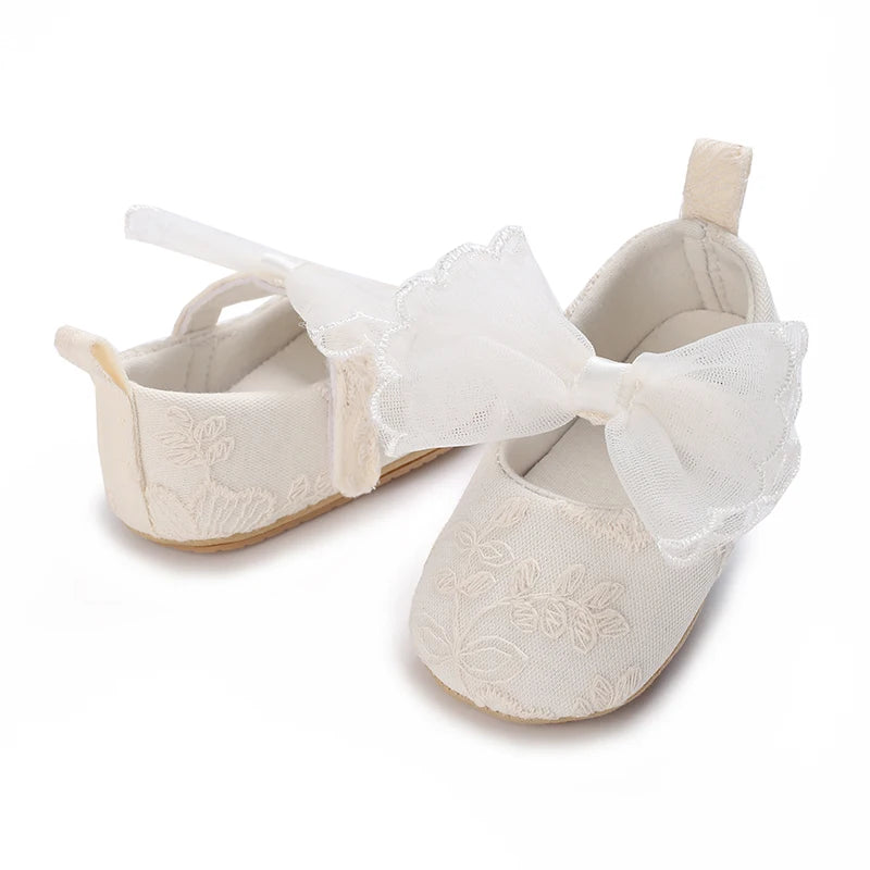 Pair of light beige lace-trimmed baby girl moccasin shoes with a bow