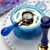 A blue wax seal melting kit with a gold heater and spoon resting on a white surface.
