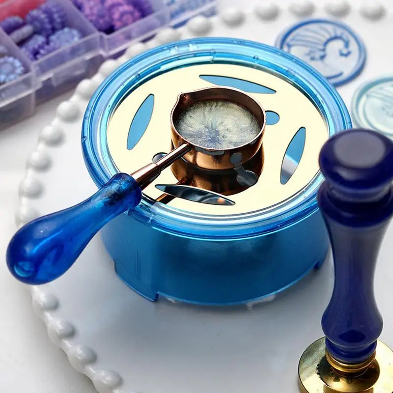 A blue wax seal melting kit with a gold heater and spoon resting on a white surface.