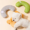 A white fluffy dog plush toy lying next to two green and gray U-shaped pet pillows.