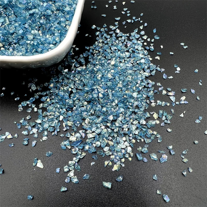 Crushed blue glass crystals scattered on a dark surface next to a small white dish.