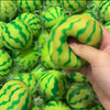 A hand is squeezing a bright green watermelon-themed squishy stress ball with a striped texture.