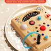 A wooden interactive circuit busy board with various buttons, lights, and switches resting on a plate.