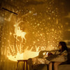 A person sits in a dimly lit room illuminated by a yellow starry projector casting light patterns on the wall.