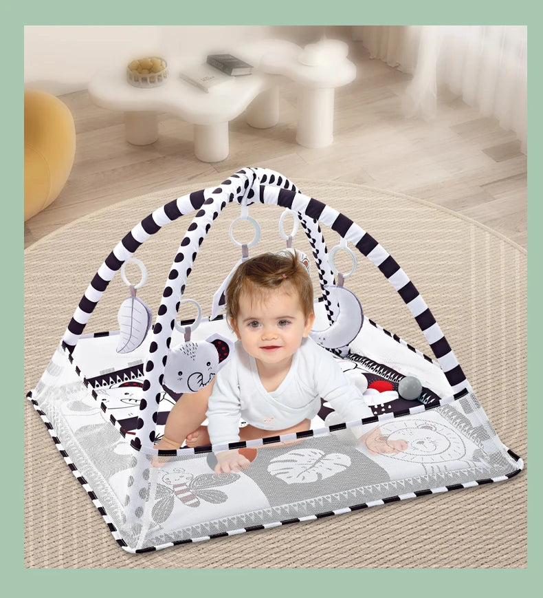A baby is sitting inside a white and black striped play mat with a fitness frame and hanging toys.