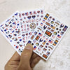 A hand holds a sheet of USA flag nail decals featuring various American flags and patriotic designs.