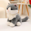 A fluffy gray and white kitten plush toy sitting on a white surface.