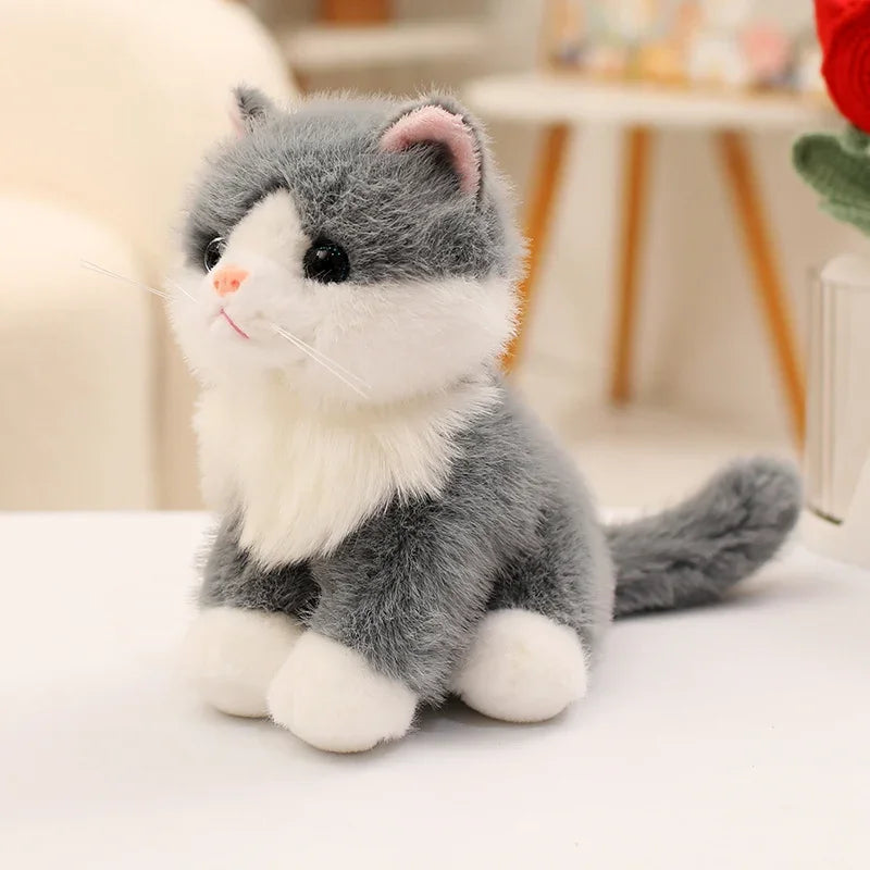 A fluffy gray and white kitten plush toy sitting on a white surface.