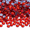 A close-up view of small, faceted red and silver glass crystal rhinestones scattered on a white surface.