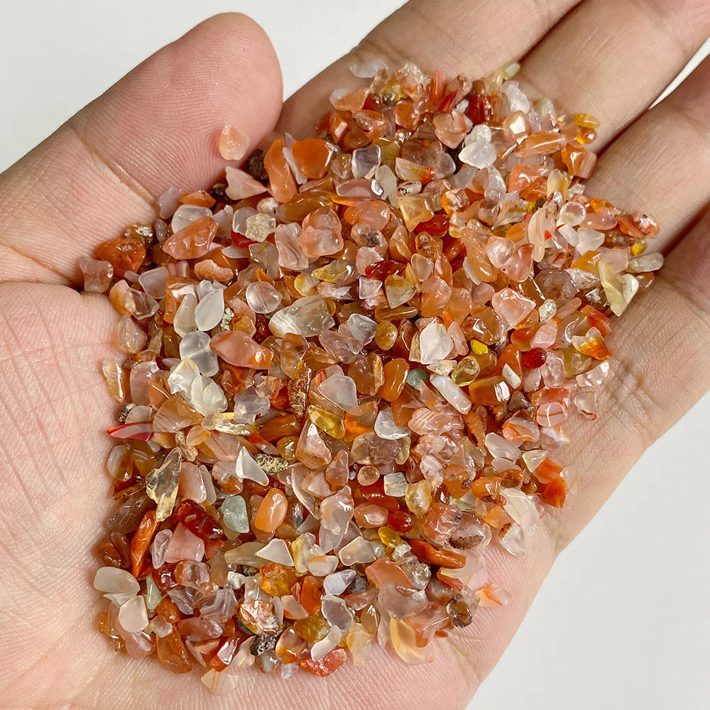 A hand holds a pile of reddish-orange and translucent natural stone chips for jewelry making