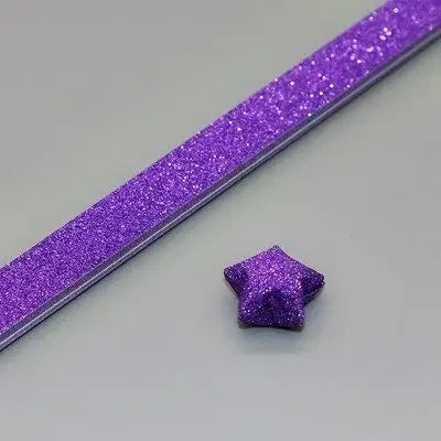 Purple glitter origami star paper strips laid diagonally on a light gray surface.