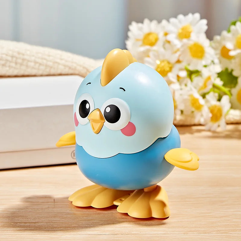 A cute blue wind-up chick toy with yellow beak and feet sitting on a wooden surface next to white and yellow flowers.