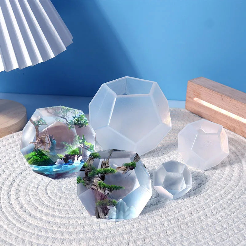 A collection of clear geometric resin casting molds shaped like polyhedrons and natural scenes on a white surface.