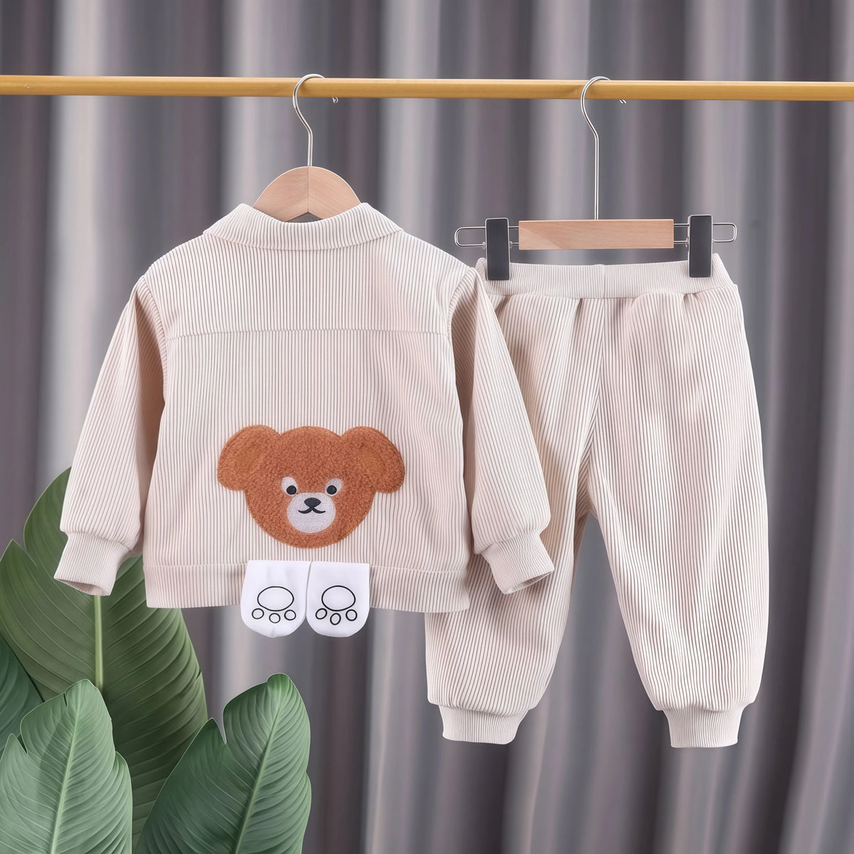 A light beige kids cartoon bear corduroy tracksuit set featuring a jacket and matching pants hanging on a wooden hanger.