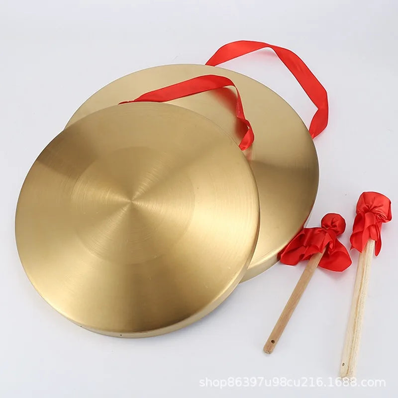 A polished gold alloy gong with a mallet and red ribbon, used for meditation or ceremonial purposes.