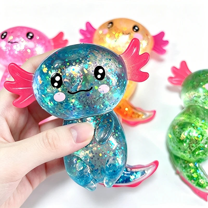 A hand holds a blue glitter axolotl squishy stress relief toy next to an orange one.