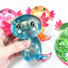 A hand holds a blue glitter axolotl squishy stress relief toy next to an orange one.