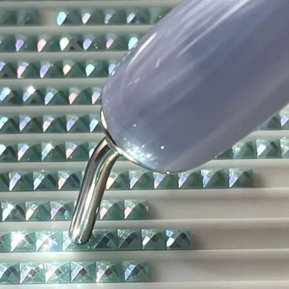 Close-up of a metal diamond painting pen tip with a purple gradient barrel and silver ferrule resting on a white surface.