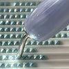 Close-up of a metal diamond painting pen tip with a purple gradient barrel and silver ferrule resting on a white surface.