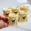 A hand holds several small, pale yellow miniature dollhouse baguette basket sets decorated with black heart drawings.