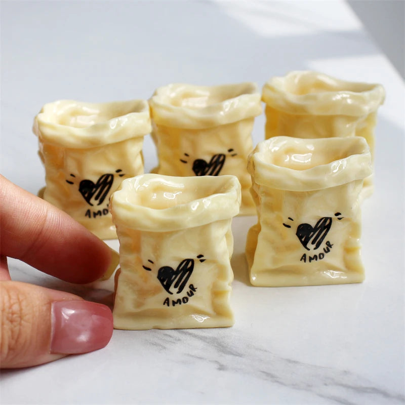 A hand holds several small, pale yellow miniature dollhouse baguette basket sets decorated with black heart drawings.