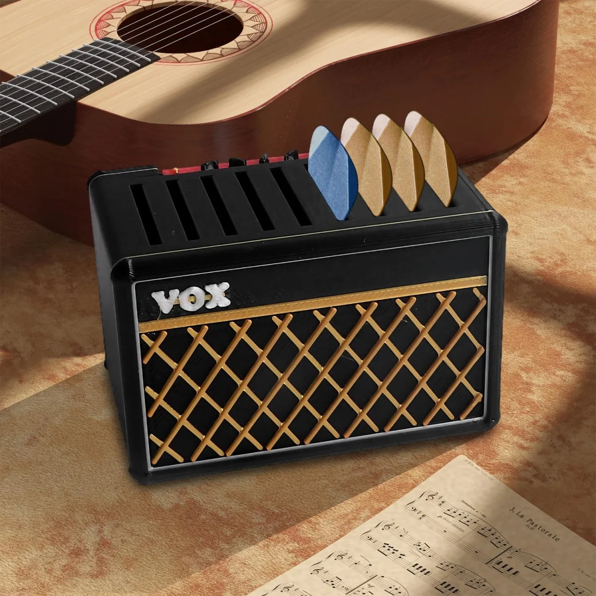 A black guitar pick holder with a speaker-shaped design featuring wooden picks resting on the top, placed on a sheet of music