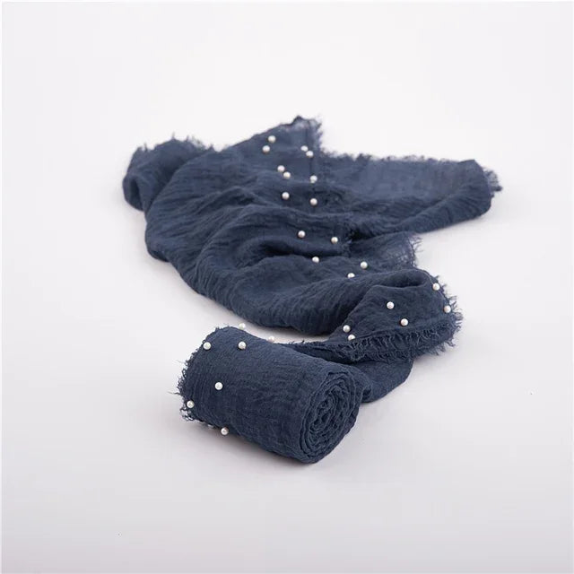 A dark navy knit wrap with pearl detailing, rolled up and draped on a white background.