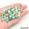 A hand holds a collection of natural stone round beads in various shades of green and white for jewelry making