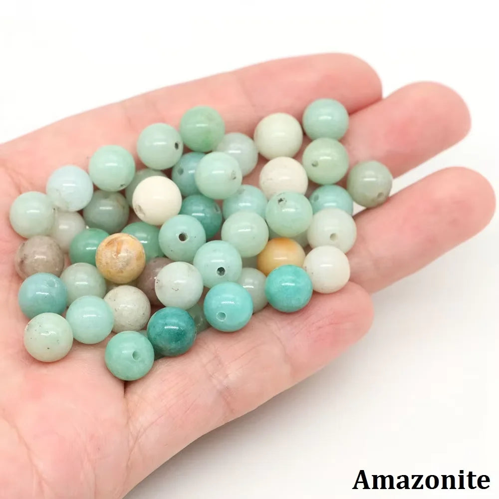 A hand holds a collection of natural stone round beads in various shades of green and white for jewelry making