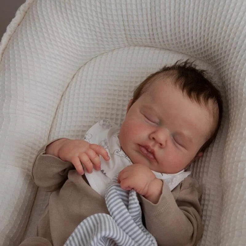 A newborn baby doll with rooted hair is sleeping inside a white, textured cradle.