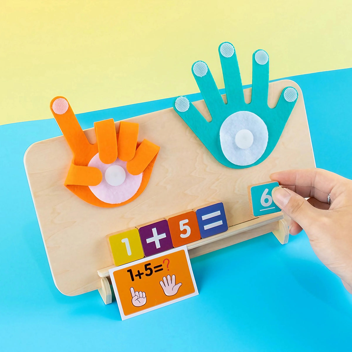 A wooden finger counting math toy showing the equation 1+5=? with colorful fingers and numbers on a light wooden board.
