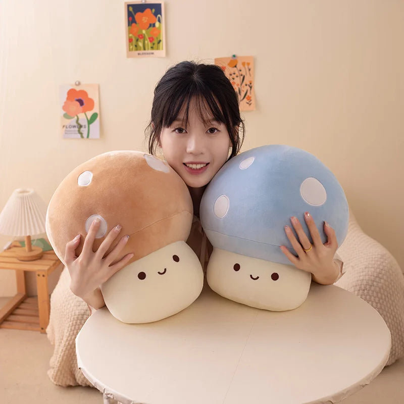 A person is holding two soft, round mushroom-shaped plush pillows in shades of brown and blue.