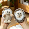 A pair of fluffy, light brown and white hedgehog plush toys held in a person's hands.