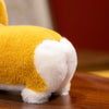 A yellow and white soft Corgi plush pillow resting on a wooden surface.