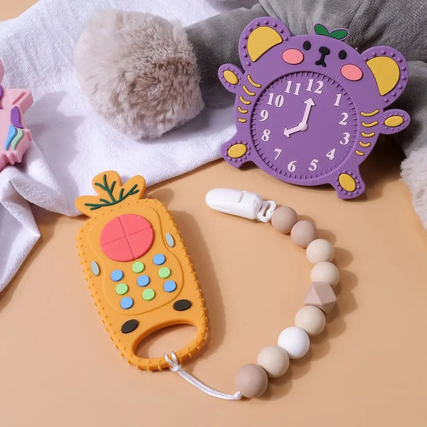 A silicone teether toy shaped like a yellow pineapple and a purple clock are displayed on a light background.