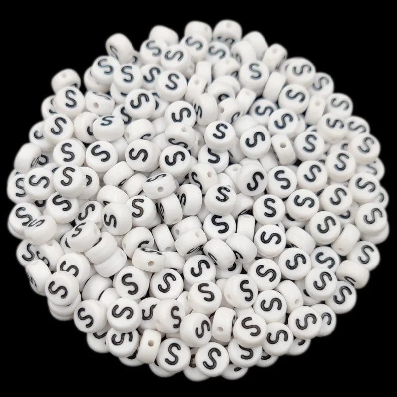 A pile of small white acrylic alphabet letter beads for jewelry making