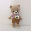 A handmade crochet stuffed bear with light brown fur, purple shirt, and brown overalls.