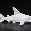 A white super soft hammerhead shark plush toy lying on a dark surface.