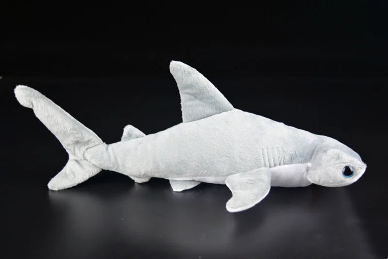 A white super soft hammerhead shark plush toy lying on a dark surface.