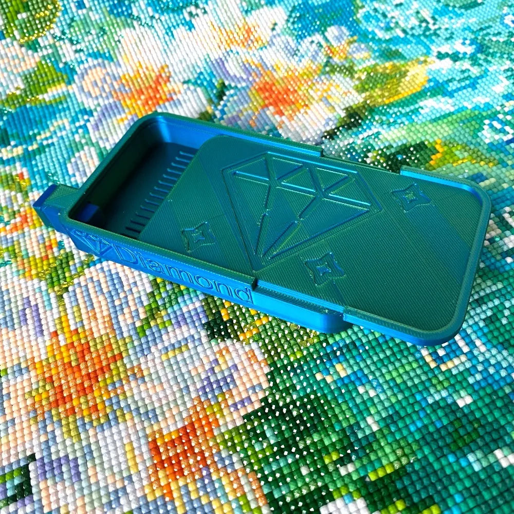 A teal diamond painting organizer tray with storage compartments placed on a colorful fabric background.