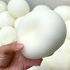A hand holds a white squishy bread stress ball, showing its soft texture and round shape.