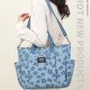 A woman holds a light blue floral canvas tote bag with multiple pockets against a neutral background.
