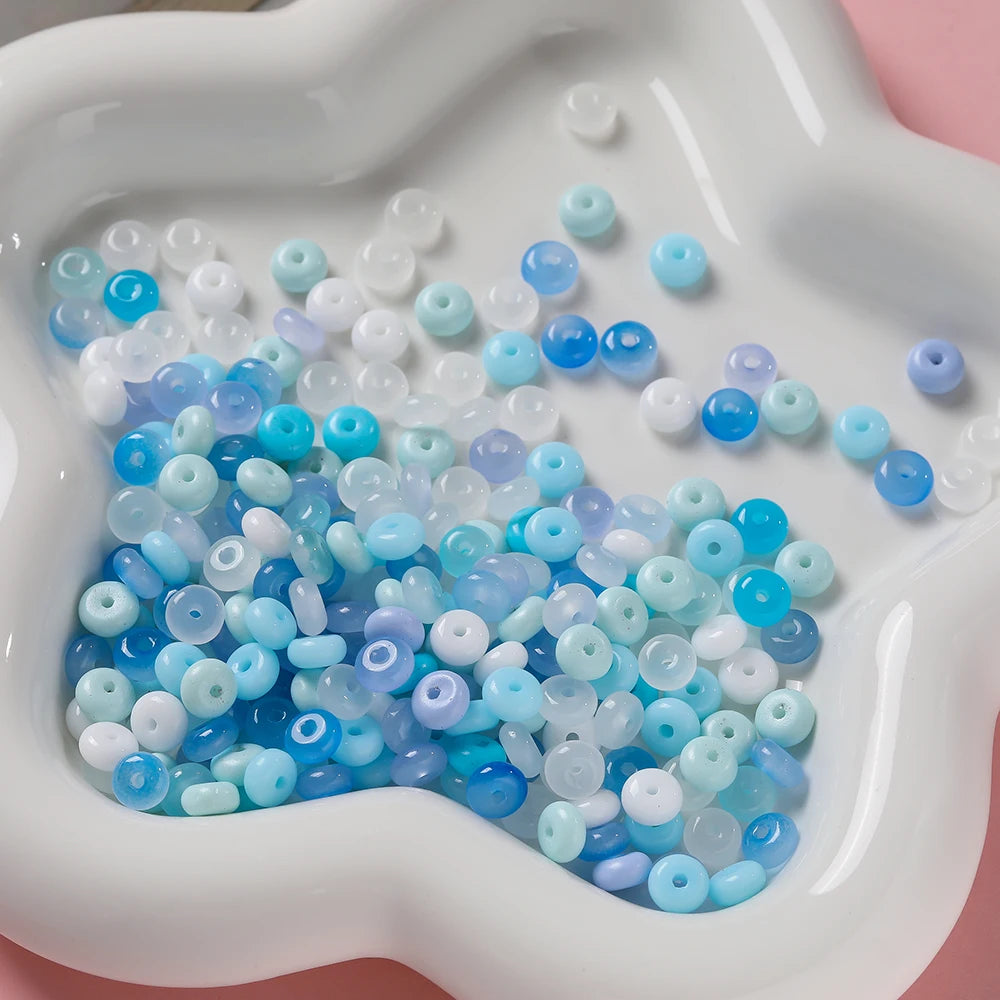 A collection of small, round glass spacer beads in various shades of blue and white are displayed in a white mold.