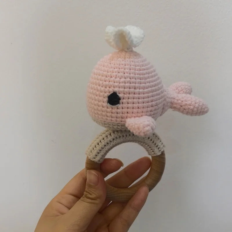 A handmade pink otter rattle and teether ring made of soft yarn, held in a hand.
