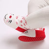 A close-up of white knitted baby winter boots with red accents and festive patterns.