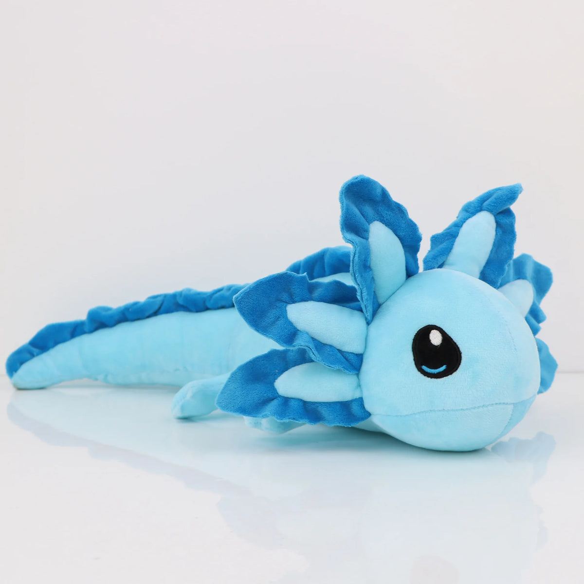 A light blue plush toy of an axolotl with spiky fins and a black eye, lying on a white surface.