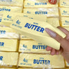 A hand holds a yellow butter squishy toy packaged in clear plastic bags.