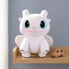 A white cartoon plush toy resembling a dragon with large blue eyes and pink accents sitting on a wooden shelf.